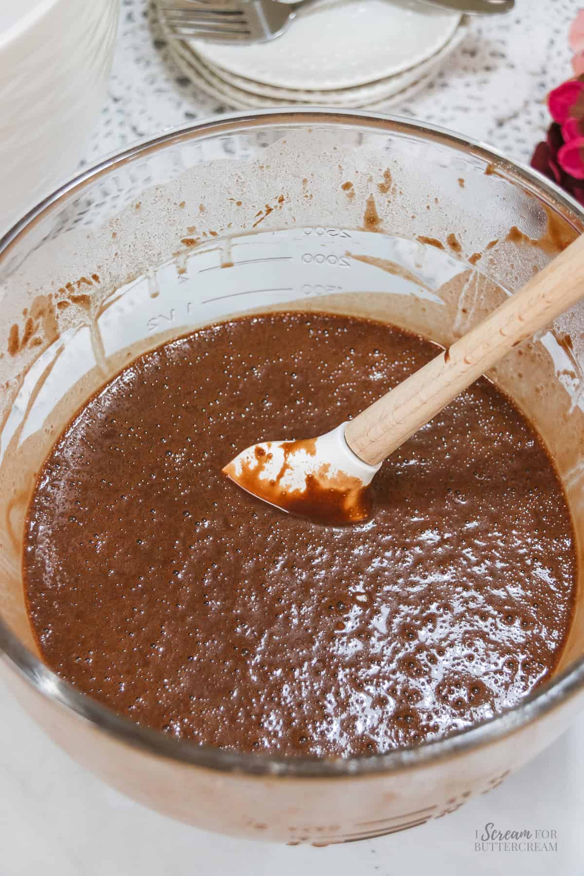 Chocolate Nutella cake batter mixed in a large glass bowl and ready to be poured into cake pans.