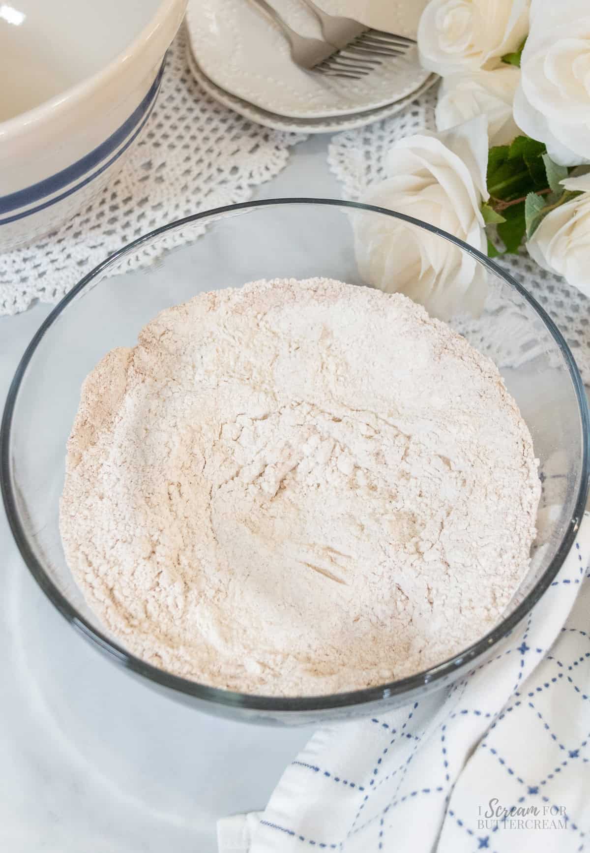 Glass mixing bowl filled with combined dry ingredients for pumpkin spice Bundt cake, including flour and warm spices.