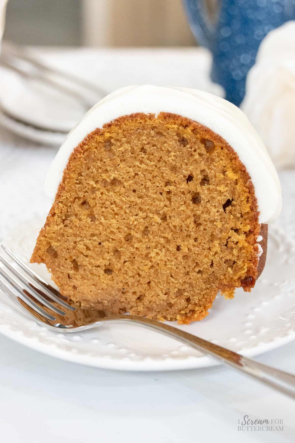 Close-up of a thick slice of moist pumpkin spice Bundt cake with a golden-brown crumb and creamy white glaze on a dessert plate.