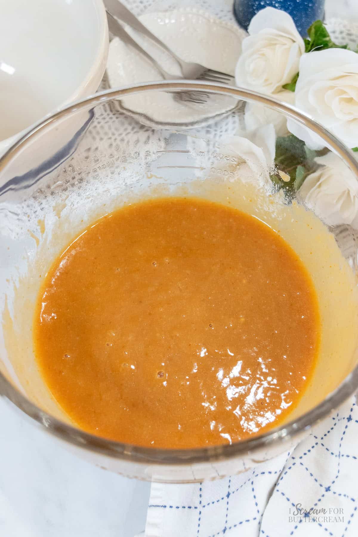 Glass mixing bowl filled with smooth orange pumpkin mixture and wet ingredients for pumpkin spice Bundt cake.