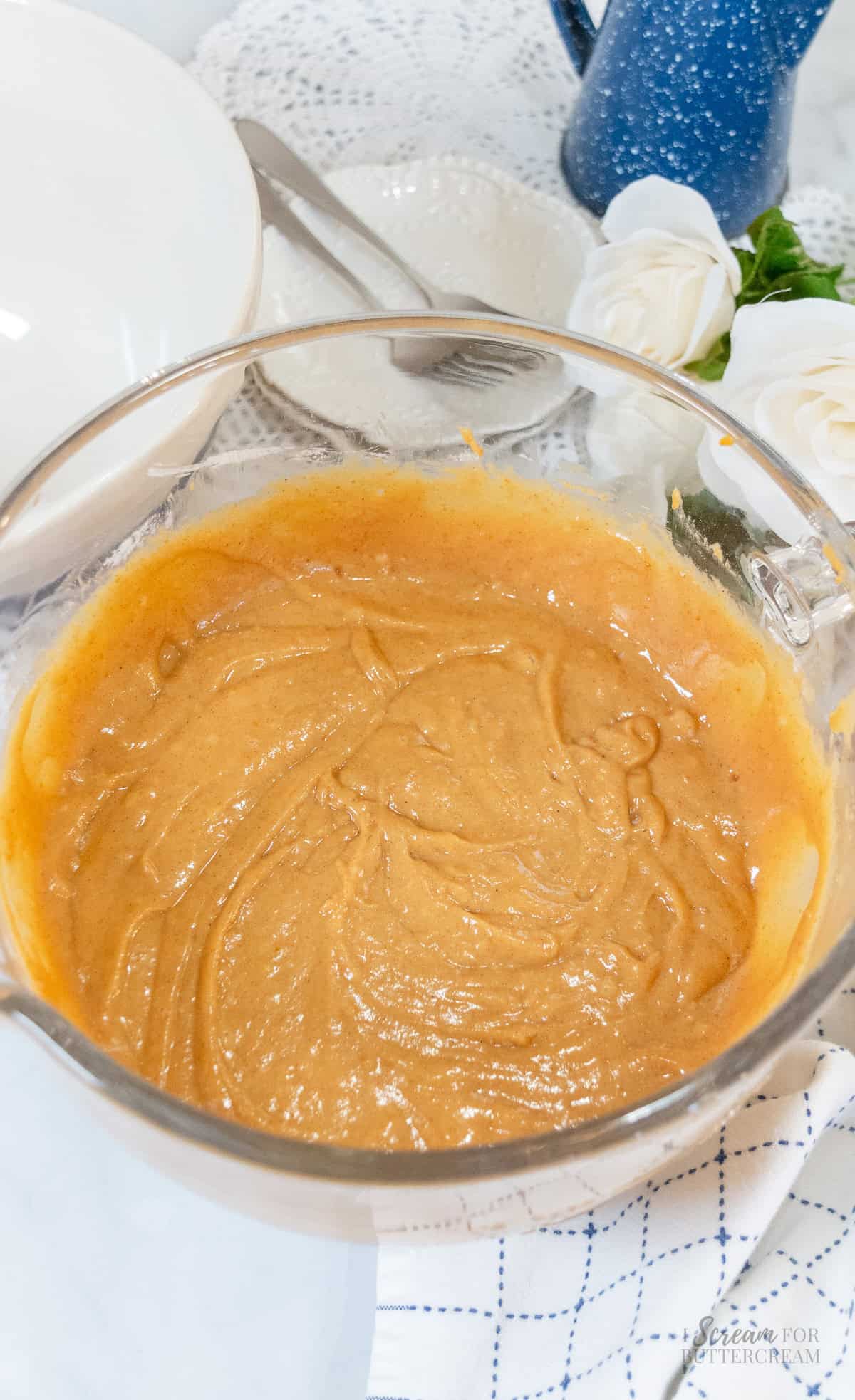 Glass mixing bowl filled with thick, smooth orange pumpkin spice Bundt cake batter, ready to pour into the cake pan.