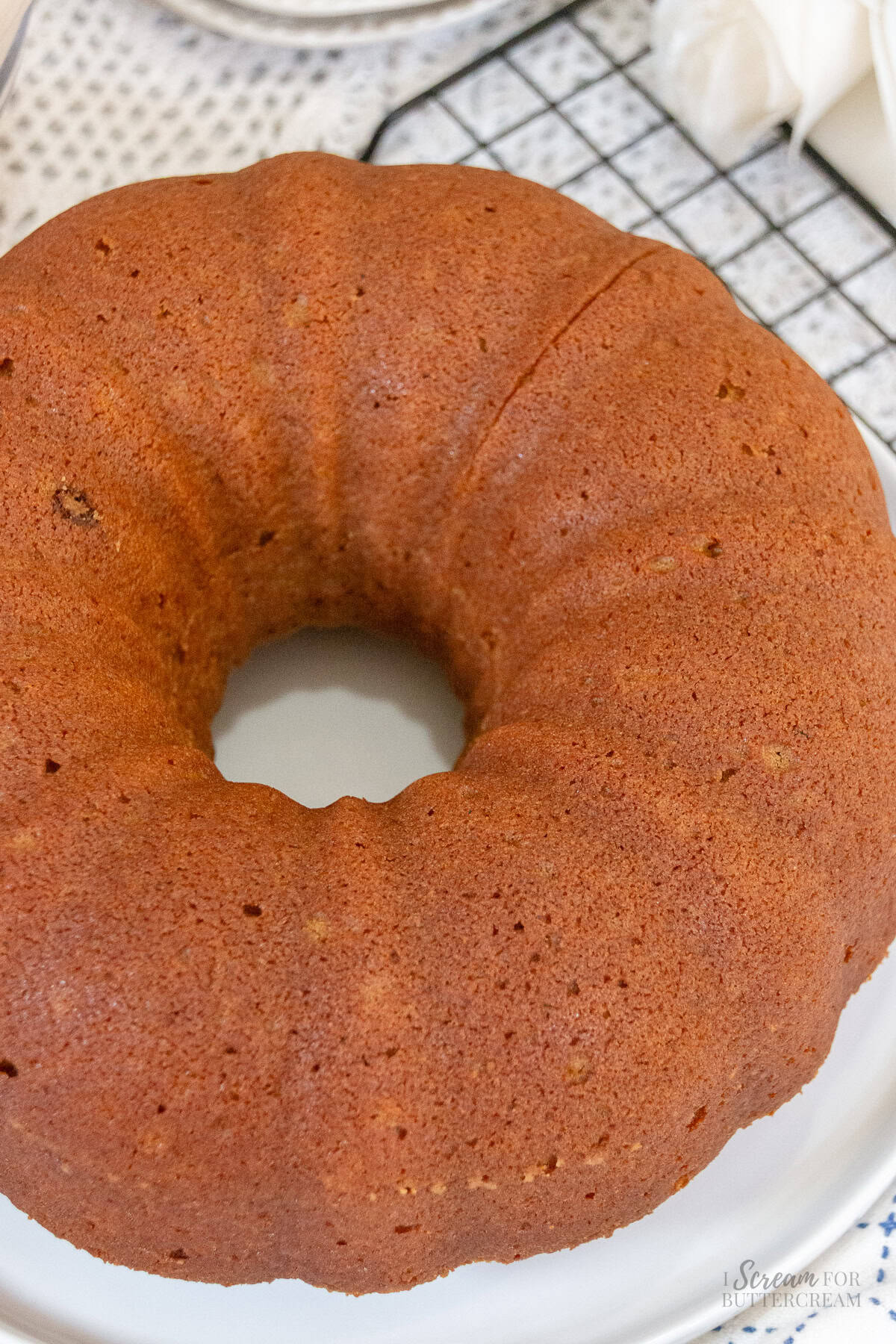 Unfrosted pumpkin spice Bundt cake with a smooth golden-brown crust on a white serving plate, ready for cream cheese glaze.