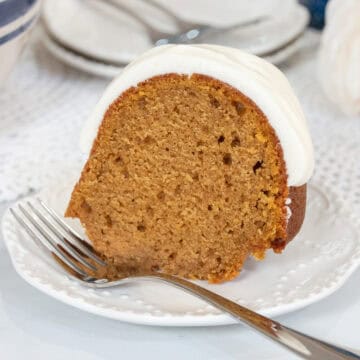 Slice of moist pumpkin spice Bundt cake topped with thick cream cheese glaze on a white dessert plate with a fork.