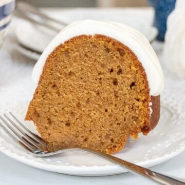 Close-up of a slice of moist pumpkin spice Bundt cake topped with thick white cream cheese glaze on a white dessert plate with a fork.